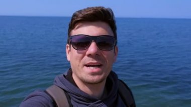Selfie adam blogger deniz plajında aboneleri ile görüşmeler, dalgalar el ve gülümsüyor.