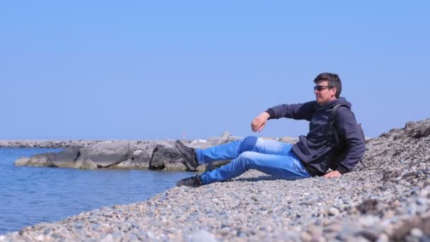 L'homme voyageur touristique vient à la plage de pierre se trouve et regarde la mer . — Video