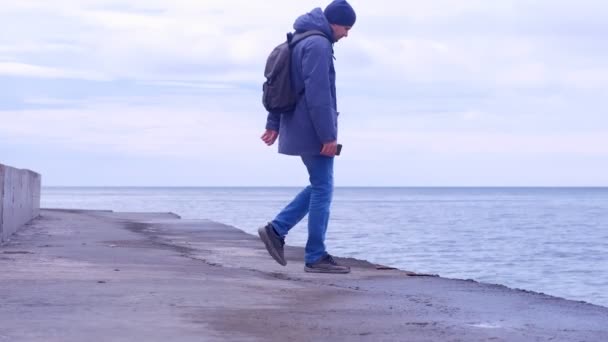 Чоловік приходить на стару морську набережну і дивиться на море взимку . — стокове відео