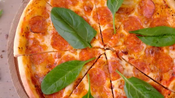 Нарізка піци салямі з листям шпинату на дерев'яній дошці, вид зверху . — стокове відео