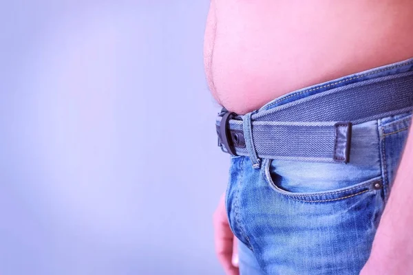 Mans fat stomach is hanging out of jeans, side view.