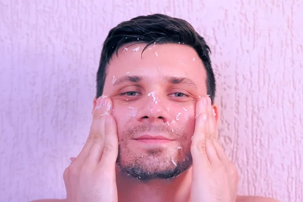 Young man is applying fresh homemade coconut mask on the face and neck. — Stock Photo, Image