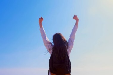 Zafer kız kazanan gökyüzü arka plan geri görünümünde ellerini kaldırarak poz.