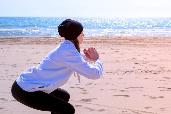 Девушка делает приседания на пляже морской песок фитнес на открытом воздухе спортивные упражнения на обучение . — стоковое фото