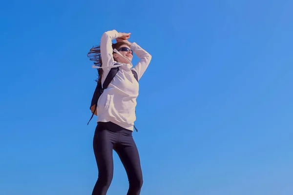 Lycklig flicka vinnare hoppar i seger pose med att höja händerna blå himmel bakgrund. — Stockfoto