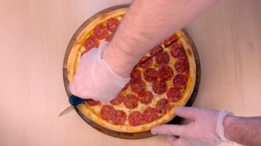 Cook salampizzayı dilimler halinde keser. lastik eldiven eller yakın çekim üst görünüm.