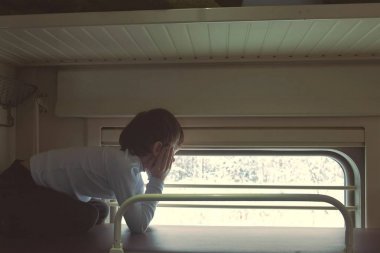 Çocuk trende ikinci sınıf bir satır boşluğu en üst rafta yalan ve penceresine bakarak. Arkadan görünüm.