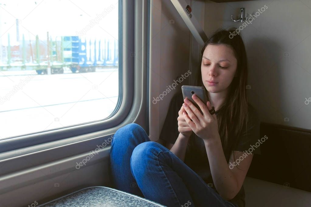 Tired young woman in train watching video in mobile phone.