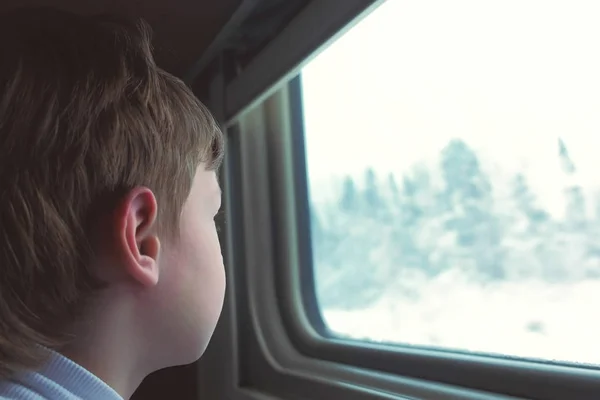Мальчик смотрит в окно в движущемся поезде на зимний пейзаж . — стоковое фото