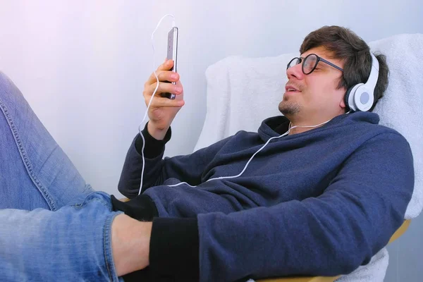 Людина слухає музику в навушниках на смартфоні і співає пісню в караоке. Розслабся час в крісло. — стокове фото