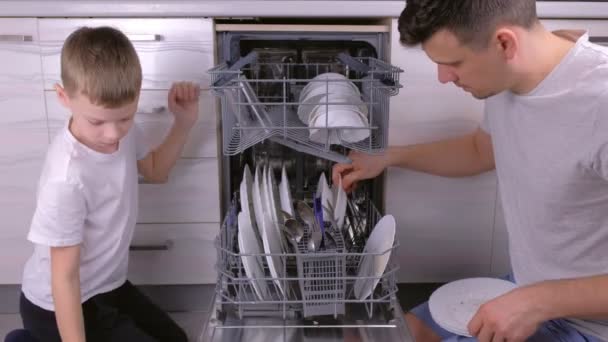 Papá e hijo están poniendo los platos en el lavavajillas juntos en la cocina . — Vídeo de stock
