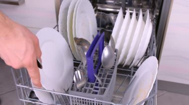 Mans el bulaşık makinesine beyaz kirli tabak ve kaşık koyarak ve mutfakta çalışıyor.
