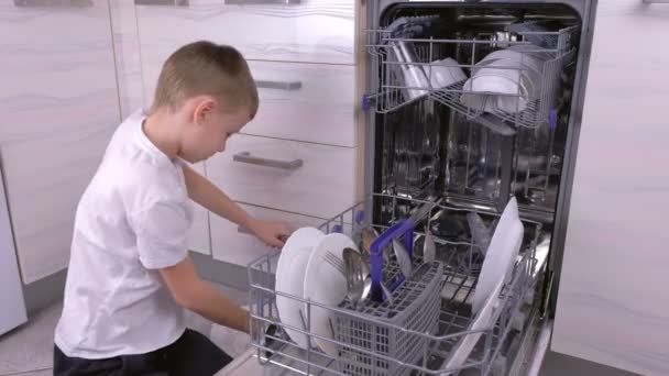 Menino está colocando uma louça na máquina de lavar louça na cozinha . — Vídeo de Stock