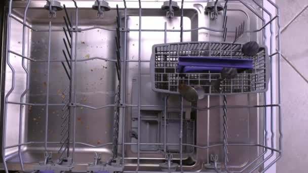 Mans hand is putting a white dirty plates and cutlery in the dishwasher basket and pushing it inside. — Stock Video