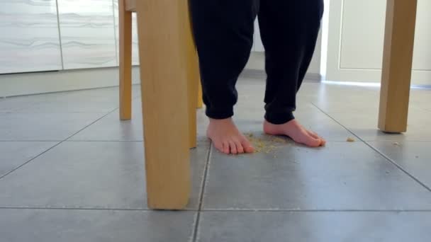 Barnet stiger upp från bordet och kliver barfota på smulorna under bordet, skakar på fötterna. Fötter närbild. — Stockvideo