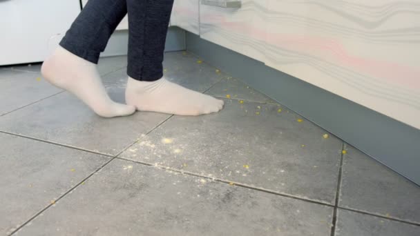 Frau geht auf den schmutzigen Fußboden in der Küche. Essensreste und Krümel fallen auf den Küchenboden. Beine in weißen Socken Nahaufnahme Seitenansicht. — Stockvideo
