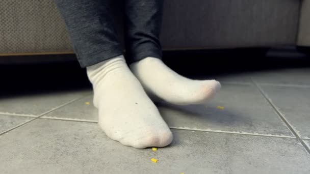 Жінка їсть на дивані і кришиться кукурудзяними пластівцями на підлозі. Ноги і підлога крупним планом . — стокове відео