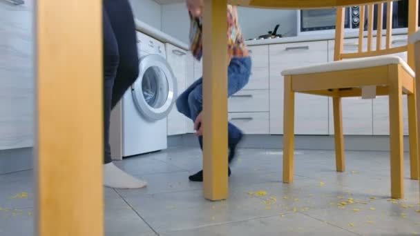 Mam scheldt haar zoon voor verspreid voedsel op de keukenvloer en maakt hem schoon te maken. Opruimen maïs vlokken van de vloer samen. — Stockvideo