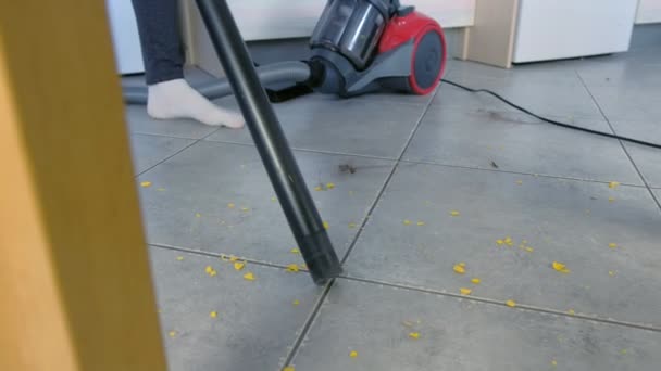 Frau staubsaugt den Küchenboden mit grauer Fliese ohne Bürste, nur Staubsaugerrohr. Beine aus nächster Nähe.