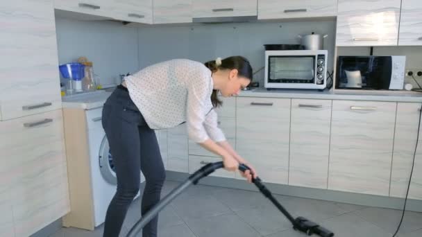 Γυναίκα σκούπισμα με ηλεκτρική σκούπα το πάτωμα της κουζίνας. Αυτή που τακτοποιεί τις νιφάδες καλαμποκιού διάσπαρτα στο πλακίδιο γκρι. — Αρχείο Βίντεο