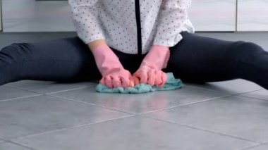 Pembe lastik eldivenli kadın mutfak zeminindeki lekeyi bir bezle yıkar ve sertçe ovalar. Yerde kiremitler var. Eller yakın çekim.