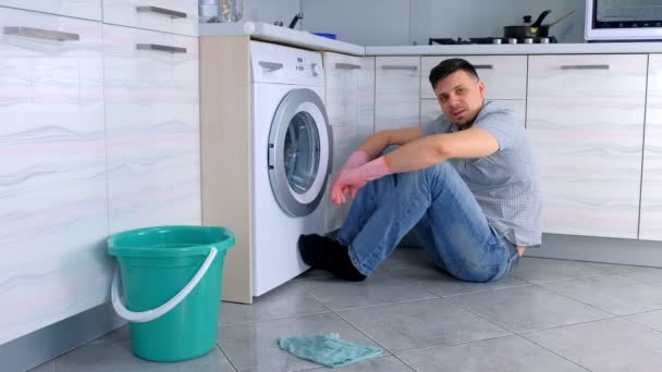 Man in rubberen handschoenen hebben een rust van het schoonmaken zittend op de keuken vloer. — Stockvideo