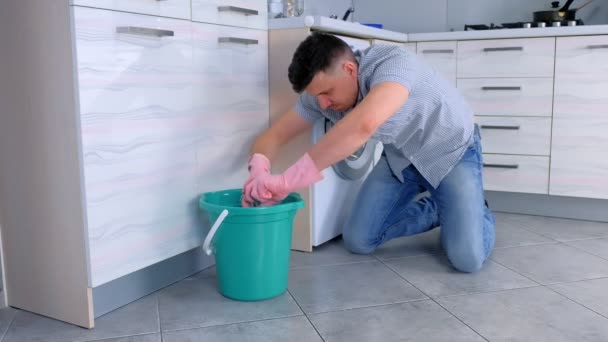Несчастный уставший мужчина в резиновых перчатках моет пол на кухне и смотрит в камеру в конце . — стоковое видео