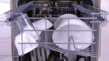 Adam bulaşık makinesi kirli beyaz tabaklar yükler, içinde sepet iter ve yakın.