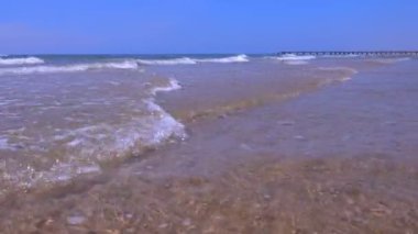 Güneşli bir günde kum plajda uzun dalgalar ve iskele ile Seascape.