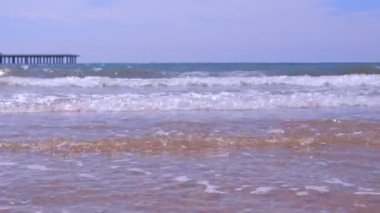 Güneşli bir günde kum plajda uzun büyük dalgalar ve iskele ile deniz kıyısı.
