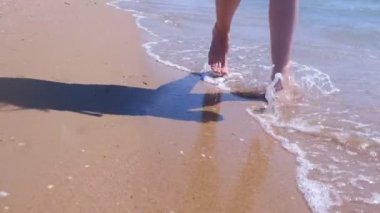 Yalınayak kadın turist bacakları deniz dalgaları kum plajda suda yürüyor.