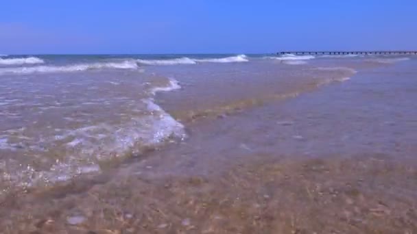 Paisaje marino con olas largas y muelle en playa de arena en un día soleado . — Vídeo de stock