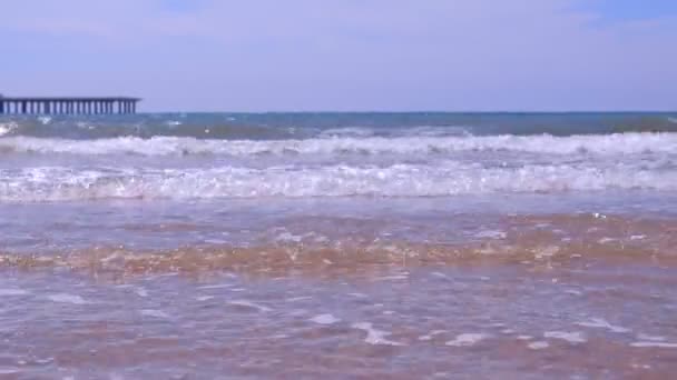 Морський берег з довгими великими хвилями і пірсом на піщаному пляжі в сонячний день . — стокове відео