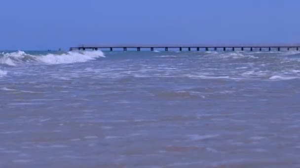Krásná modrá pozadí s dlouhými zpěněné vlny a molo. — Stock video