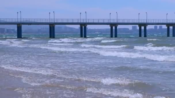 Vista sobre el mar con olas muelle ciudad costera y montañas en el día soleado . — Vídeo de stock