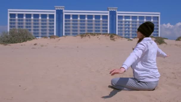 Une voyageuse sur la plage jette du sable qui vole dans le vent par une journée ensoleillée . — Video