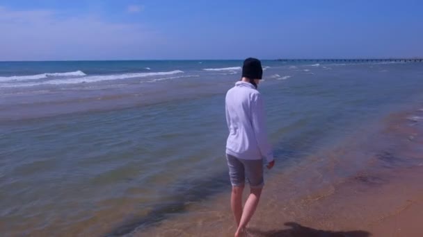 Femme marche à l'eau de mer sur la plage de sable hors saison porte en sweat à capuche et chapeau . — Video