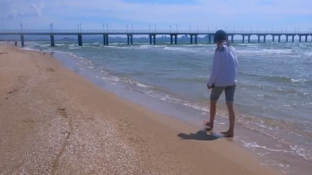 Donna scalza cammina al molo sulla spiaggia sabbiosa in ventosa giornata di sole in mare . — Video Stock