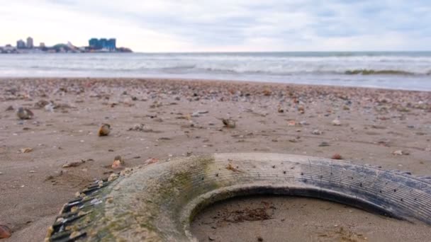 Neumático de coche arrojado por las olas en la orilla arenosa durante una tormenta. Neumático cubierto de conchas marinas . — Vídeos de Stock