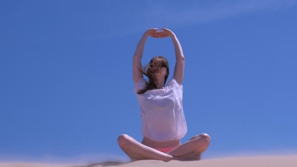 Woman stretching sits lotus pose sandy beach summer vacation hands up windy day. — Stock Video