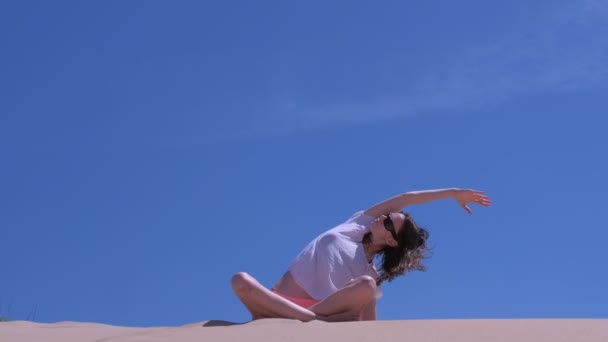 Woman stretch sits lotus pose sandy beach tilts in side yoga practice windy sky. — Stock Video