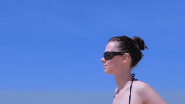 Portrait de jeune femme en lunettes de soleil sur fond bleu ciel, vue de côté . — Video