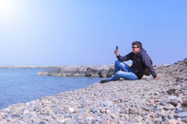 Onun akıllı telefon adam görüşmeler görüntülü sohbet tatilde deniz taş plajda oturur.