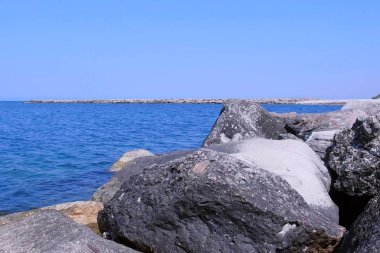 Berrak güneşli bir günde büyük taşlar, iskele ve mavi su ile Seascape.