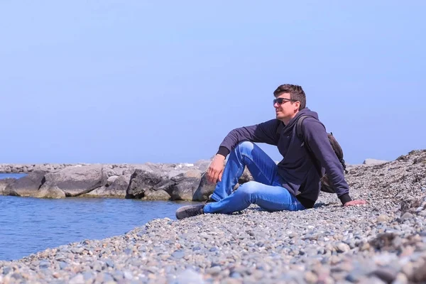 Happy man Tourist Traveller sitter vid Stone Beach och tittar på havet på semester. — Stockfoto