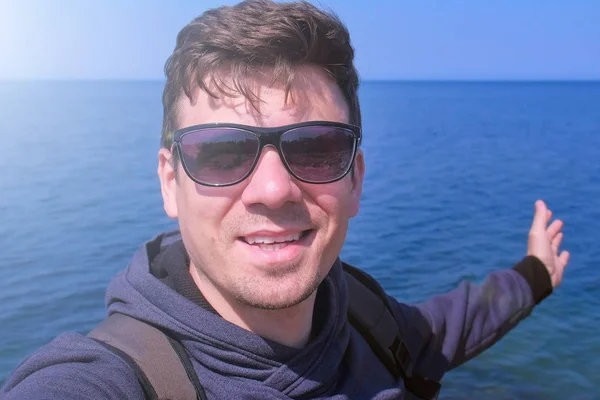 Man video chats selfie smartphone op zee strand golven hand begroet en glimlacht. — Stockfoto