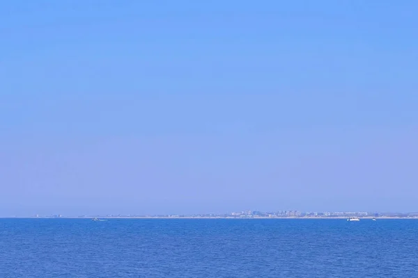 Θαλασσινό φόντο με γαλάζια νερά, γιοτ, πόλη σε απόσταση και καθαρό ουρανό. — Φωτογραφία Αρχείου