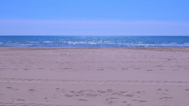Θάλασσα άμμος παραλία με μπλε νερό και αφρώδη κύματα την ηλιόλουστη μέρα. — Αρχείο Βίντεο
