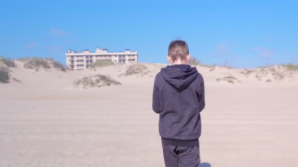 Menino está andando na praia de areia para dunas de areia vista para trás atividades ao ar livre . — Vídeo de Stock