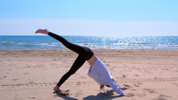 Woman does Downward Facing Dog pose in yoga on sea sand beach sport exercise. — Stock Video